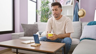 Genç İspanyol bir adam akıllı telefondan evde kahve içerken görüntülü arama yapıyor.
