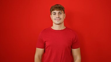 İzole edilmiş kırmızı arka planda ciddi bir ifadeyle duran İspanyol genç adam.