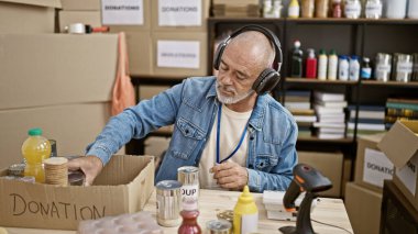 Bald man with headphones volunteers at a charity in a warehouse, organizing canned food donations clipart