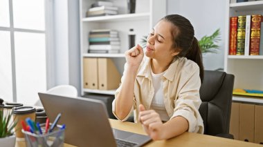 Neşeli, kendine güveni tam genç İspanyol kadın güzel ofis içinde dizüstü bilgisayarda çalışırken müzik eşliğinde dans ediyor.