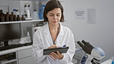 Young beautiful hispanic woman scientist using touchpad at laboratory