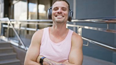 Gülümseyen, dövmeli, kulaklıklı, şehir ortamında müziği seven genç bir adam..