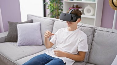 Gülümseyen genç bir çocuk modern oturma odasındaki bir koltukta sanal gerçeklik kulaklığı takarak gençliğini ve teknolojisini ifade ediyor..