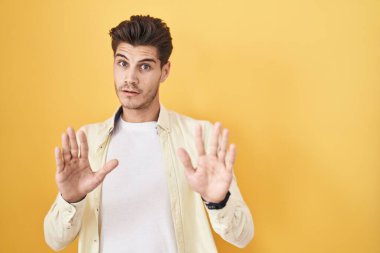 İspanyol genç adam sarı arka planda duruyor. Avuçlarını hareket ettiriyor. Korkmuş ve iğrenç bir ifadeyle reddediyor. Dur ve yasakla. 