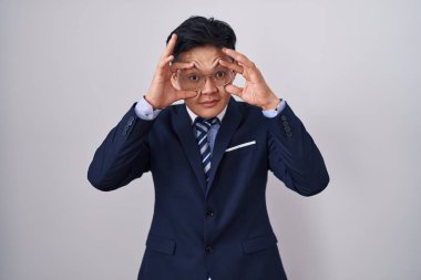 Genç Asyalı takım elbiseli ve kravatlı adam parmaklarıyla gözlerini açmaya çalışıyor, uykulu ve yorgun sabah yorgunluğu çekiyor. 