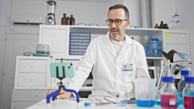 Beyaz saçlı orta yaşlı bilim adamı laboratuardaki video görüşmesi sırasında tıbbi araştırmalardan bahsediyor.