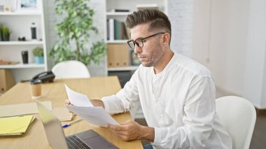 Yakışıklı İspanyol profesyonel ofis masasında kritik belgeleri okumaya dalmış, ciddi ve konsantre görünüyor.