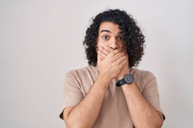 Beyaz arka planda duran kıvırcık saçlı İspanyol adam yanlışlıkla ağzı ellerle kapatmış. gizli kavram. 