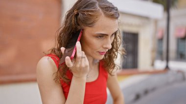 Ciddi bir konsantrasyonda kaybolmuş çekici genç bir kadın, akıllı telefonundan soğuk bir şekilde bir sesli mesaj dinliyor, güneşin altında işlek bir şehir sokağında duruyor..