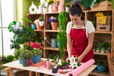 Young beautiful hispanic woman florist make bouquet of flowers at flower shop