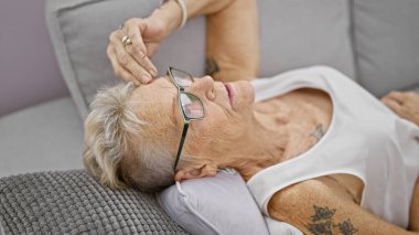 Stresli, gri saçlı, son sınıf öğrencisi kadın evdeki oturma odasındaki kanepede tek başına yatıyor, üzüntüden, hayal kırıklığından ve endişeden tükenmiş bir şekilde zihinsel sağlık krizi belirtileri gösteriyor..