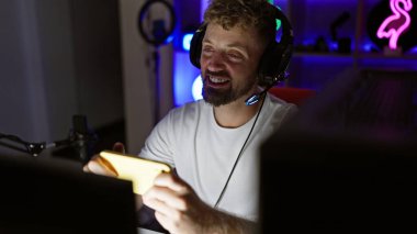 Sakallı, yakışıklı, beyaz bir adam gecenin bir yarısı karanlık bir odada kulaklık takıp oyun oynuyor..