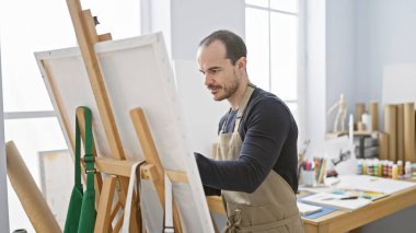 Parlak bir sanat stüdyosundaki tuvale önlük takmış kel bir adam..