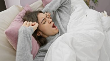 Genç bir İspanyol kadın yatakta esniyor, yatak odasında rahat bir sabah tasvir ediyor..