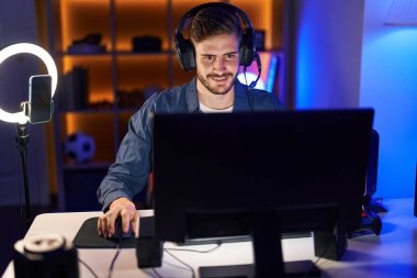 Genç beyaz adam oyun odasında bilgisayar kullanarak video oyunu oynuyor.