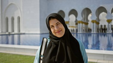 Tesettürlü genç bir İspanyol kadın Abu Dabi Camii 'nin su ve karmaşık mimarisinin önünde duruyor..