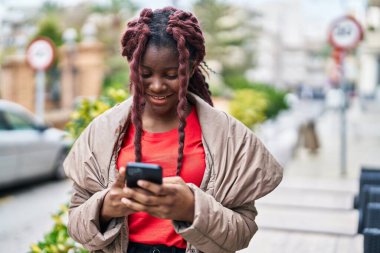 Afro-Amerikalı kadın sokakta akıllı telefon kullanarak kendine güveniyor.