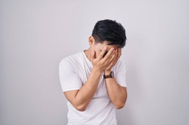 Beyaz arka planda duran Asyalı genç adam, ağlarken yüzünü ellerle kapatan üzgün bir ifadeyle. depresyon kavramı. 