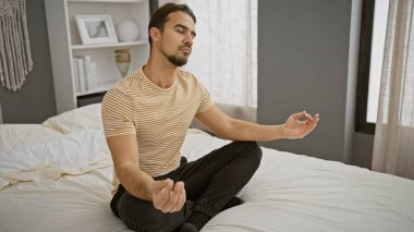Genç bir İspanyol adam, modern bir yatak odasındaki bir yatakta huzur içinde meditasyon yapıyor. Huzur ve sükunet gösteriyor..