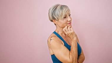 Gri kısa saçlı, düşünceli, olgun bir kadın pembe izole bir arka plana poz veriyor. Güzellik ve olgunluğu temsil ediyor..