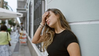 Endişeli genç İspanyol kadın, şehir sokaklarında duvarlara yaslanmış, güneşli havanın altında şüpheyle bakan bir portresi.