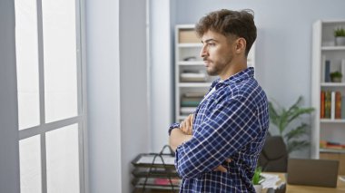 Çaba sarf etmeden zarif, genç bir Arap hiç şüphesiz düşünceli, işçi duruşu, kollarını kavuşturmuş, ofis penceresinden dışarı bakıyor. Bir sorunla mı karşı karşıya yoksa bir fikir mi üretiyor??