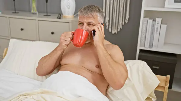 Grauhaariger Mann Trinkt Kaffee Bett Während Einem Modernen Schlafzimmer Telefoniert — Stockfoto