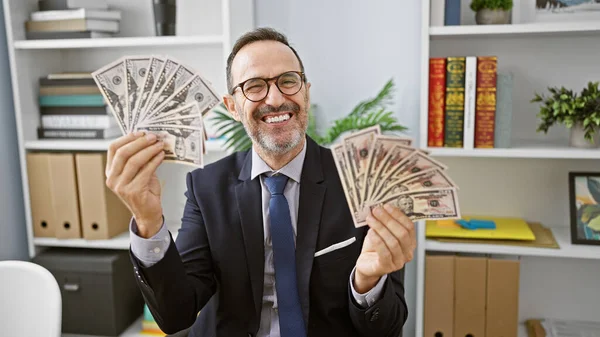 Cheerful middle age man with grey hair, successful business worker, grinning while counting his dollar wealth in the office