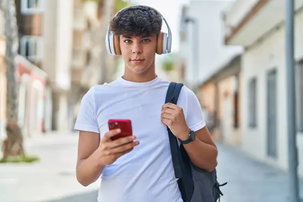 Young hispanic teenager student smiling confident listening to music at street