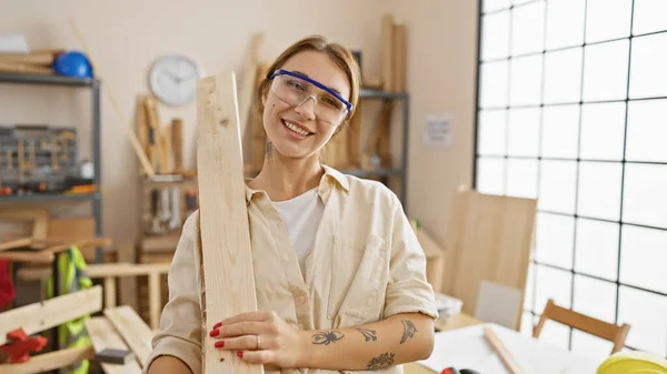 Uśmiechnięta Kobieta Okularach Ochronnych Trzyma Drewno Jasnym Warsztacie Stolarskim — Zdjęcie stockowe
