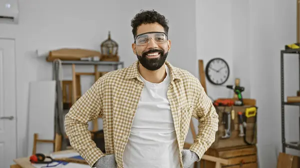 身穿安全护目镜 留着胡子的英俊年轻人自信地微笑在一个木制品工作室里 — 图库照片