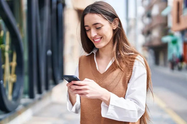 Genç, güzel, İspanyol bir kadın sokakta akıllı telefon kullanarak gülümsüyor.