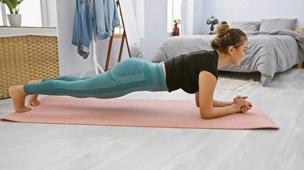 Genç, zinde İspanyol bir kadın, odasında sıkı antrenman yapıyor ve sıkı çalışıyor, tamamen konsantre olmuş, atletik vücudu parıldıyor, rahat yatak odasında ilham verici bir fitness portresi oluşturuyor.