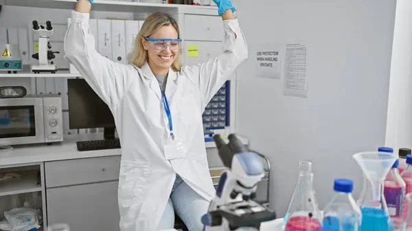 A joyful young woman scientist celebrates in a laboratory setting, surrounded by equipment and chemicals, highlighting innovation and success.