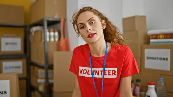 A young woman wearing a \'volunteer\' t-shirt poses confidently in a donation center with boxes and supplies in the background.