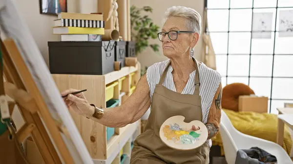 Mature, grey-haired female artist fully immersed in her art, diligently drawing at her indoor studio, a quiet person embodying creativity and concentration