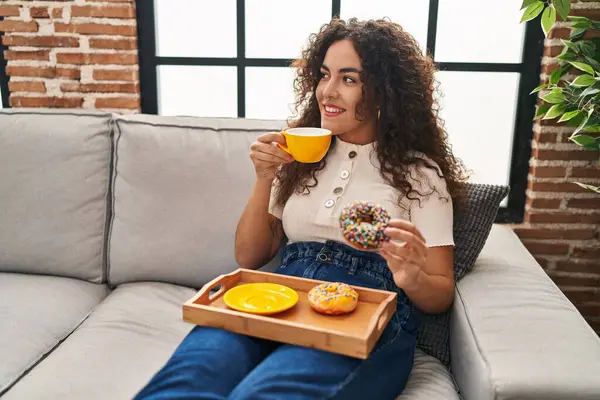Genç, güzel, İspanyol bir kadın kahvaltısını evde, koltukta yapıyor.