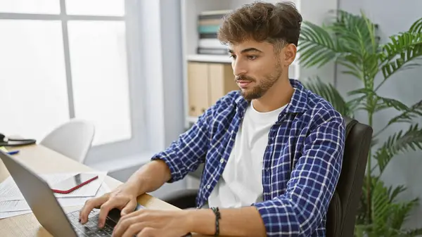 Handsome young arab man, a relaxed yet serious and elegant business pro, working hard in his indoor office space, concentrating on his laptop for success