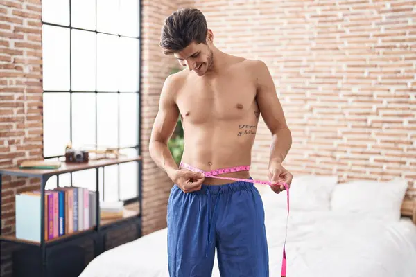 Young Hispanic Man Using Tape Measure Measuring Waist Looking Positive — Stock Photo, Image