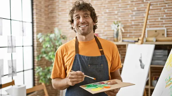 Smiling hispanic man painting in a bright art studio, exuding creativity and artistic flair.