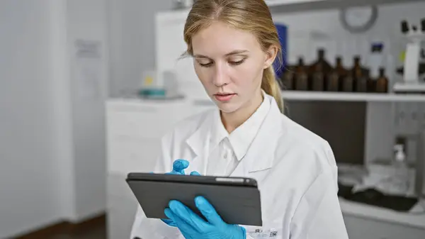 Blonde Woman Lab Coat Focuses Intently Tablet Scientific Laboratory Surrounded — Stock Photo, Image