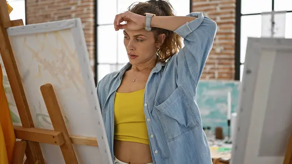 一位在画室里心事重重的年轻女画家用手在额头上摆姿势 凝视着她的画 — 图库照片