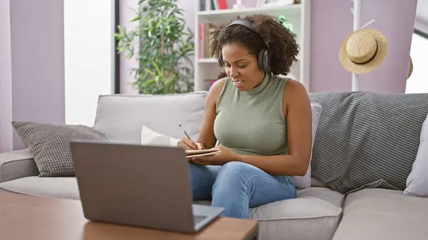 在家里用笔记本电脑在笔记本上书写辫子的非裔美国妇女 — 图库照片