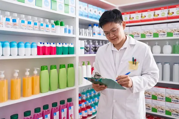 Young chinese man pharmacist writing on document at pharmacy