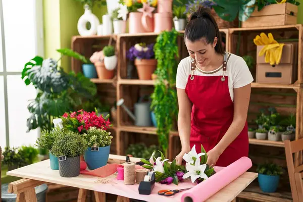 Young beautiful hispanic woman florist make bouquet of flowers at flower shop