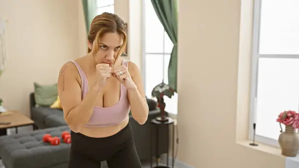 A determined woman practicing boxing moves in a spacious living room, exuding confidence and fitness.