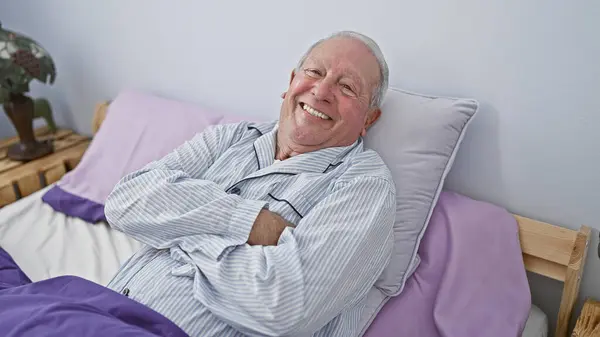 Neşeli son sınıf öğrencisi, gri saçlı ve kendinden emin, rahat bir yatak odasında kollarını kavuşturmuş, rahat bir sabahta pijamalarıyla keyfine bakıyor.