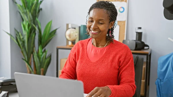 Smiling African Woman Bright Red Sweater Working Laptop Modern Office — Stock Photo, Image