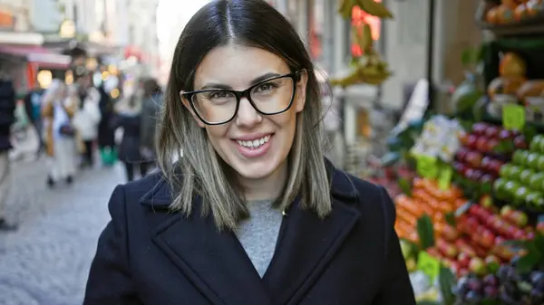 İstanbul 'da bir meyve pazarının önünde duran, gözlüklü, gülümseyen esmer kadın, şehir turizmini canlandırıyor..