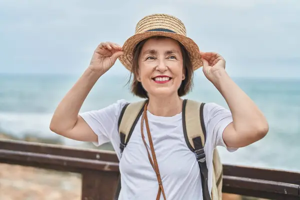 Middle age woman tourist smiling confident wearing backpack at seaside
